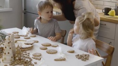 Anne çocukları öpüyor. Bir erkek ve bir kız kurabiyelerde şekerli korseli zencefilli ekmek yerler. Noel ağacının yeni yıl süslemeleri..