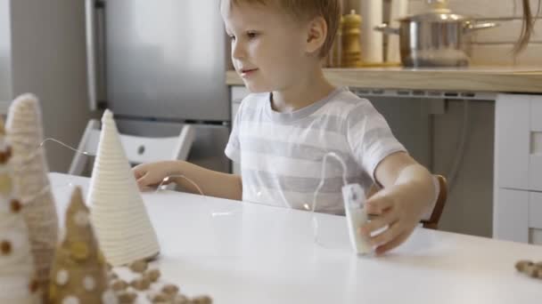 Een Jongetje Zit Aan Tafel Met Kerstversiering Tak Van Een — Stockvideo