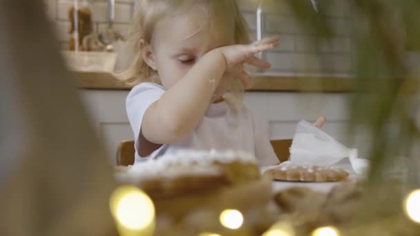 可爱的小女孩在厨房吃圣诞姜饼 一个女孩在饼干上涂了糖霜 涂上了玉米粒 圣诞树上的糖果装饰树枝 — 图库视频影像