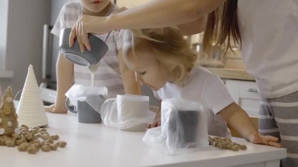 Mom and children decorate Christmas gingerbread at home. A boy and a girl paint with cornets with sugar icing on cookies. New Year's kitchen decorations branches of a Christmas tree. — Stock Footage Mom Children Decorate Christmas Gingerbread Home Boy Girl Paint Cornets Stock Footage