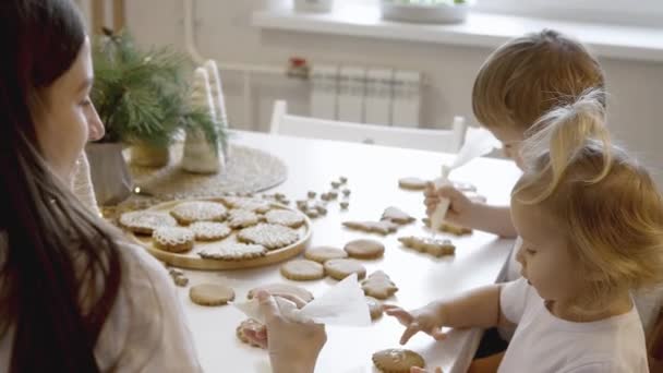 엄마와 아이들은 집에서 크리스마스 진저브레드를 장식합니다 소녀가 과자에 설탕을 코넷으로 — 비디오
