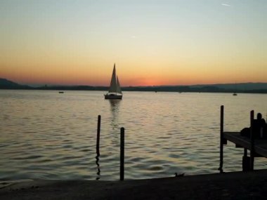 İsviçre 'nin Zugersee şehrindeki Zug Gölü manzarası, gün batımında ve bir yelkenli ile sakin.