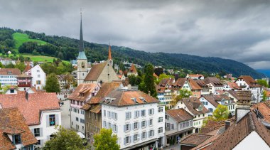 İsviçre 'nin eski Zug şehrinin arka planında yeşil tepeler ve bulutlu gökyüzü olan panoramik manzarası.