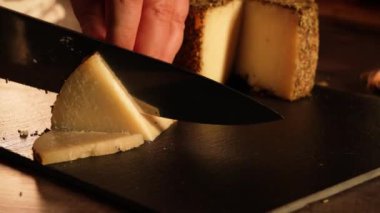 Full HD 'de 32 saniyelik video, el kamerası. Peynir kesme işlemi karanlık bir tahtada otlarla yapılır..