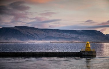 Günbatımında Norveç Denizi 'nin panoramik manzarası. Arka planda dağlar ve ön planda sarı bir deniz feneri var..