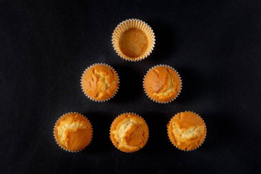 Kaplardan birinin boş olduğu, karanlık bir arka planda, üçgen şeklinde yerleştirilmiş bir grup kap kekle dolu bir hayat..