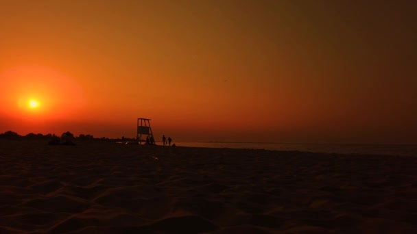 Torre Salvavidas Siluetada por la puesta del sol. Gente caminando. playa — Vídeos de Stock