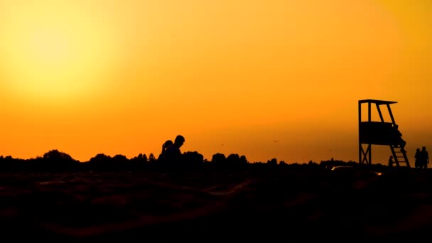 Sommarresekoncept. Mörk siluett, ikonisk retro trä livräddare vakttorn mot solnedgången orange himmel. Kontrast vakttorn kontur, strand skymning estetik. Människor — Stockvideo