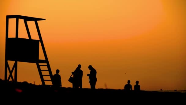 Summertime reisconcept. Donker silhouet, iconische retro houten strandwacht toren tegen zonsondergang oranje hemel. Contrast uitkijktoren omtrek, strand schemering esthetisch. Mensen — Stockvideo