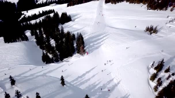 Luftaufnahme des Skigebiets mit Snowboardern den Hügel hinunter. Archivmaterial. Überfliegen der Ski- oder Snowboardbahn auf weißem Schnee, umgeben von dichtem Wald im Winter, Reisen und Sport — Stockvideo
