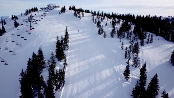 スキー場のケーブルウェイでドローンからのパノラマのトップビュー。マウンテンリゾートの雪の冬の斜面にスキーヤーやスノーボーダーを運ぶスキーリフトエレベーター、多くの人々。UHD 4kビデオ — ストック動画