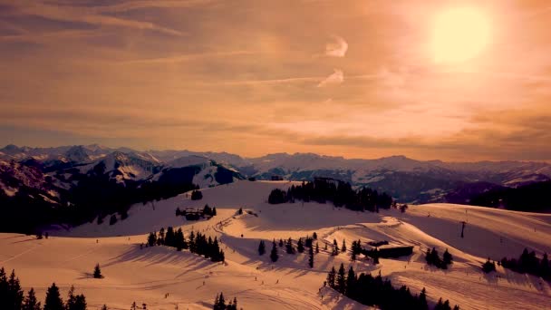 Pistas de montanha brancas pitorescas cobertas com florestas de pinheiros e pistas de esqui e teleférico em movimento na vista aérea do pôr-do-sol. Alpes — Vídeo de Stock