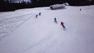 Tepenin aşağısında snowboard yapan insanların olduğu kayak merkezinin havadan görüntüsü. Stok görüntüleri. Kış mevsiminde sık ormanlarla çevrili beyaz kar üzerinde kayak pistinde uçmak, seyahat ve spor