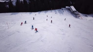 Tepenin aşağısında snowboard yapan insanların olduğu kayak merkezinin havadan görüntüsü. Stok görüntüleri. Kış mevsiminde sık ormanlarla çevrili beyaz kar üzerinde kayak pistinde uçmak, seyahat ve spor