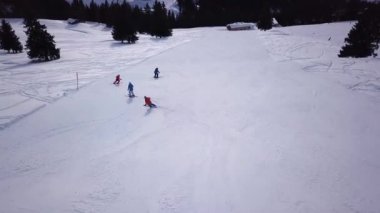 Tepenin aşağısında snowboard yapan insanların olduğu kayak merkezinin havadan görüntüsü. Stok görüntüleri. Kış mevsiminde sık ormanlarla çevrili beyaz kar üzerinde kayak pistinde uçmak, seyahat ve spor
