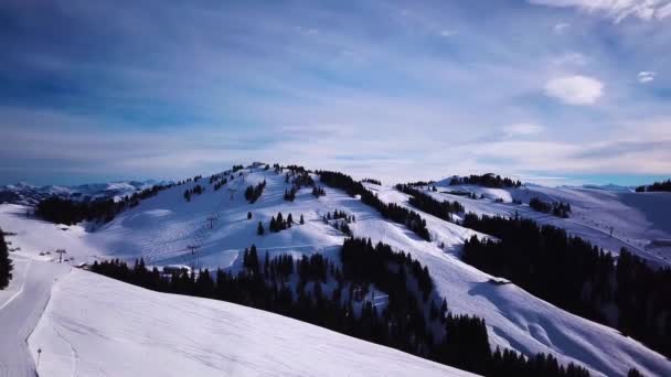 Widok z lotu ptaka na ośrodek narciarski z ludźmi na snowboardzie w dół wzgórza. Materiał filmowy. Latanie nad torem narciarskim lub snowboardowym na białym śniegu otoczonym gęstym lasem w sezonie zimowym, podróże i sport — Wideo stockowe
