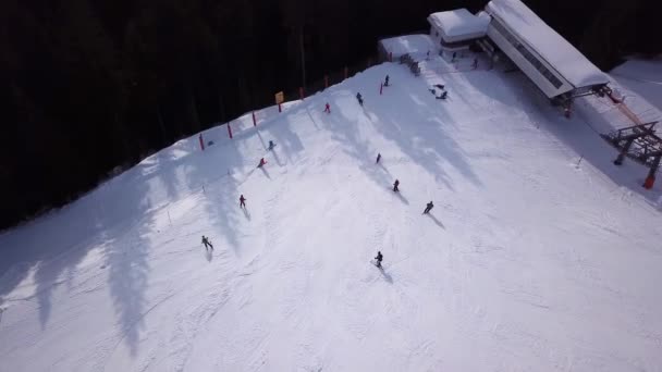 Widok z lotu ptaka na ośrodek narciarski z ludźmi na snowboardzie w dół wzgórza. Materiał filmowy. Latanie nad torem narciarskim lub snowboardowym na białym śniegu otoczonym gęstym lasem w sezonie zimowym, podróże i sport — Wideo stockowe