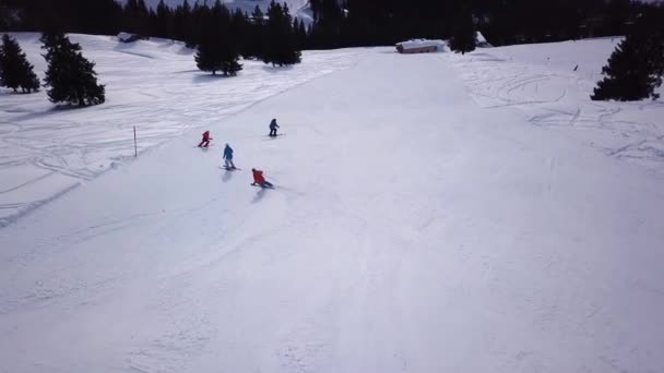 Aerial view of ski resort with people snowboarding down the hill. Stock footage. Flying over the ski or snowboard track on white snow surrounded by dense forest in winter season, travel and sport — Stock Video