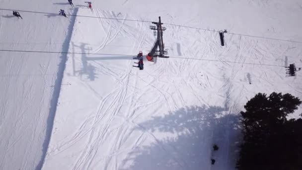 Flygfoto ovanifrån av skidstolslyften. Få personer för transport i skidorten. Skidåkare och snowboardåkare på snöiga skidbacken. Drone flyger över Cabine och publiken hiss linbana vinter vår fjäder berg — Stockvideo