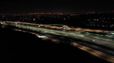 Gece şehir yollarının tepesinde hava manzaralı arabalar var. Geceleri modern gökdelenleri olan şehir manzarası. Görkemli şehir manzarası trafik otobanlı neon fenerlerle aydınlatılıyor. Sinematik araç manzarası