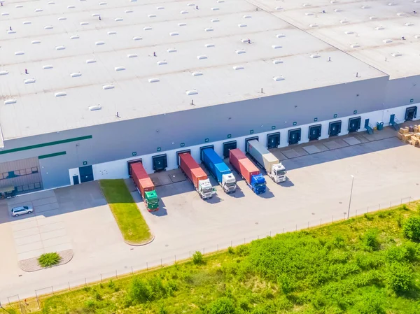 Aerial view of a logistics park with warehouse, loading hub and many semi trucks with cargo trailers standing at the ramps for load/unload