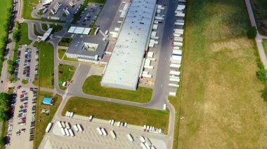 Trucks with semi-trailers stand on the parking lot of the logistics park with loading hub and wait for load and unload goods at warehouse ramps at sunset. Aerial view