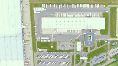 Aerial top down view of the big logistics park with warehouses, loading hub and a lot of semi trucks with cargo trailers awaiting for loading/unloading goods on ramps