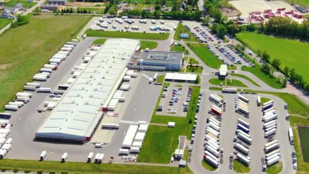 Trucks with semi-trailers stand on the parking lot of the logistics park with loading hub and wait for load and unload goods at warehouse ramps at sunset. Aerial view — стоковое видео