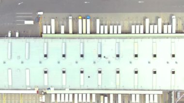 Aerial top down view of the big logistics park with warehouses, loading hub and a lot of semi trucks with cargo trailers awaiting for loading/unloading goods on ramps