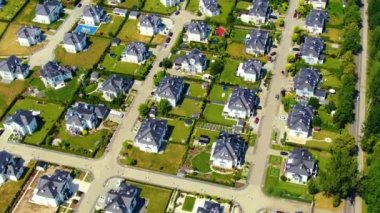 Street with new homes in spring season. Single family houses and residential construction planned community. Aerial from backyard to front exterior reveal as car drives by.