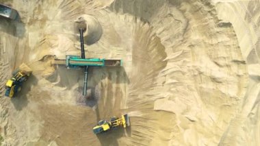 Önünde kova olan tekerlek doldurucusu ezicide taş, hava aracı atışı. Taş ocağında, kum ve çakıl gibi yapı malzemeleri üretimi için ekipmanla çalışan ağır makineler.