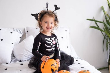 Cadı kostümlü güzel bir kız elinde balkabağı, süslemeli yatak odasında fener tutuyor..