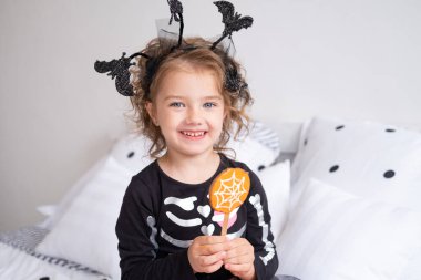 Cadılar Bayramı için dekore edilmiş cadılar bayramı kostümlü güzel kız kurabiye yiyor..