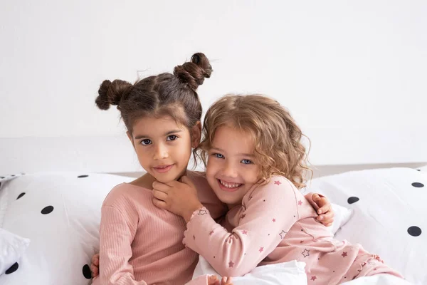 Dwa Piękne Różnorodne Dzieci Dziewczyny Piżamie Przytulając Się Łóżka Nowoczesnym — Zdjęcie stockowe