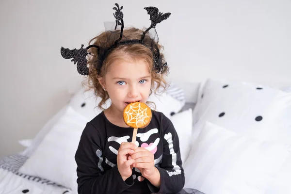 Gyönyörű kislány boszorkány jelmezben eszik cookie-kat díszített halloween hálószoba — Stock Fotó