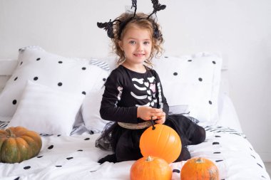 Cadı kostümlü güzel bir kız elinde balkabağı, süslemeli yatak odasında fener tutuyor..