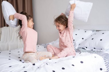 İki çocuk pijamalı, yastık savaşı yapan modern, parlak bir dairede.