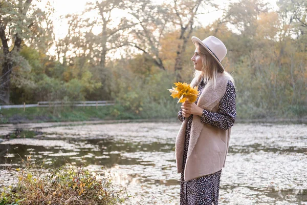 Bela jovem mulher elegante em chapéu detém folhas de outono, passeios na natureza no parque de outono no outono — Fotografia de Stock