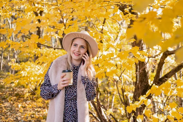 Νεαρή Γυναίκα Μοντέρνα Ρούχα Και Καπέλο Πίνοντας Καφέ Χρησιμοποιώντας Τηλέφωνο — Φωτογραφία Αρχείου