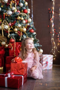 Noel ağacının yanında hediye kutusuyla güzel elbiseli, gülümseyen sarışın kız.