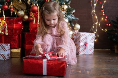 Noel ağacının yanında hediye kutusuyla güzel elbiseli, gülümseyen sarışın kız.