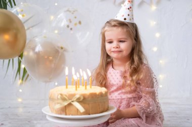 Küçük tatlı kız doğum günü pastasında mum üflüyor ve doğum gününü kutluyor.