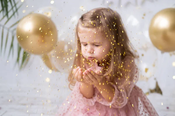 Niña feliz con el pelo largo en vestido rosa soplando confeti y celebrando su cumpleaños — Foto de Stock