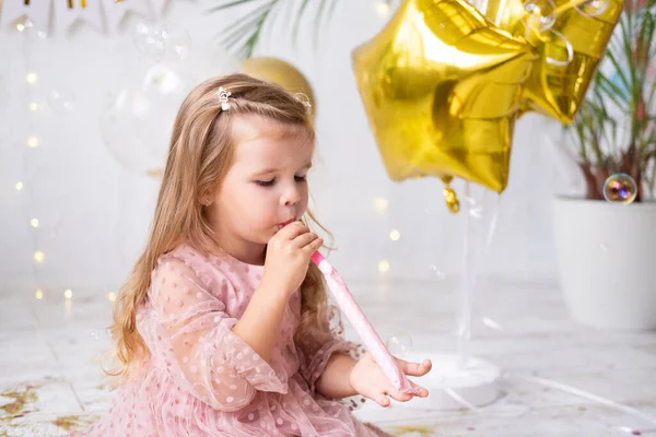 Menina feliz criança com cabelos longos em vestido rosa soprando no apito e celebrando seu aniversário — Fotografia de Stock