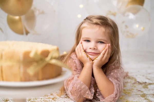 Милая маленькая девочка лежит на полу рядом торт день рождения, улыбаясь, празднуя день рождения — стоковое фото