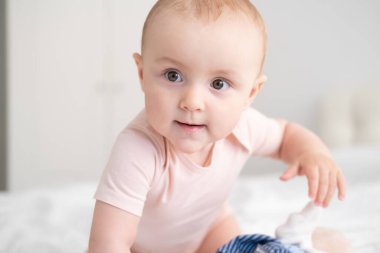 Bebek portresi. Açık pembe bir elbise içinde 10 ay. Yatakta beyaz bir yatak.