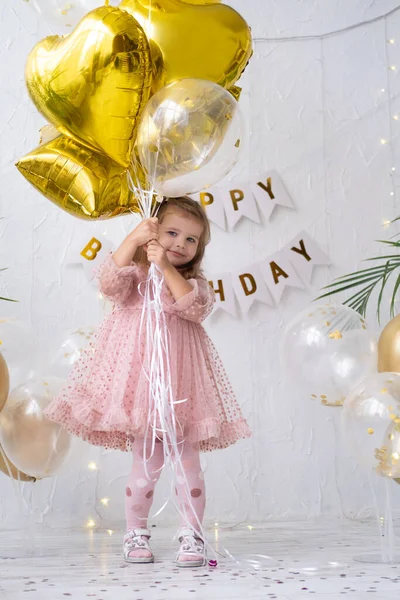 Feliz niña rubia en vestido rosa sosteniendo globos y celebrando su cumpleaños —  Fotos de Stock
