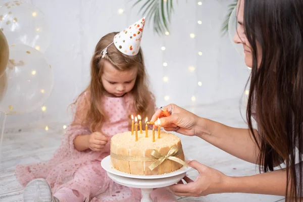 Mom lights candles on birthday cake to cute little child girl — Stock Photo, Image