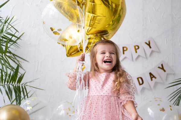 Menina loira feliz em vestido rosa segurando balões e celebrando seu aniversário — Fotografia de Stock