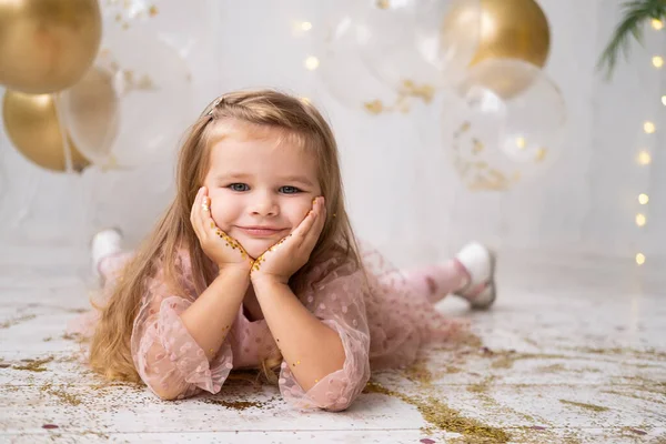 Fröhliches Kindermädchen in rosa Kleid liegt mit Konfetti auf dem Boden und feiert ihren Geburtstag — Stockfoto